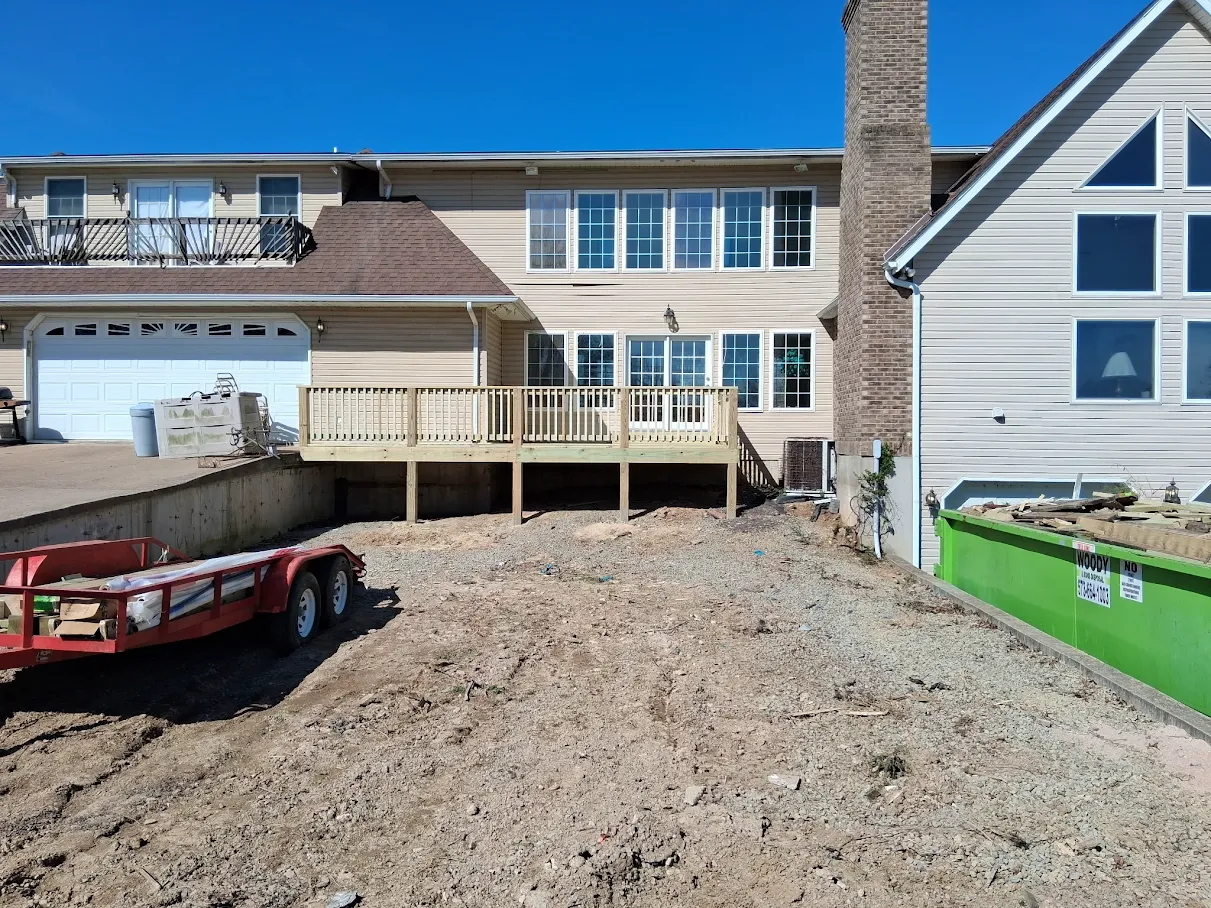Rear of a tan-sided home with a new ground-level wooden deck, two-car garage, and brick chimney