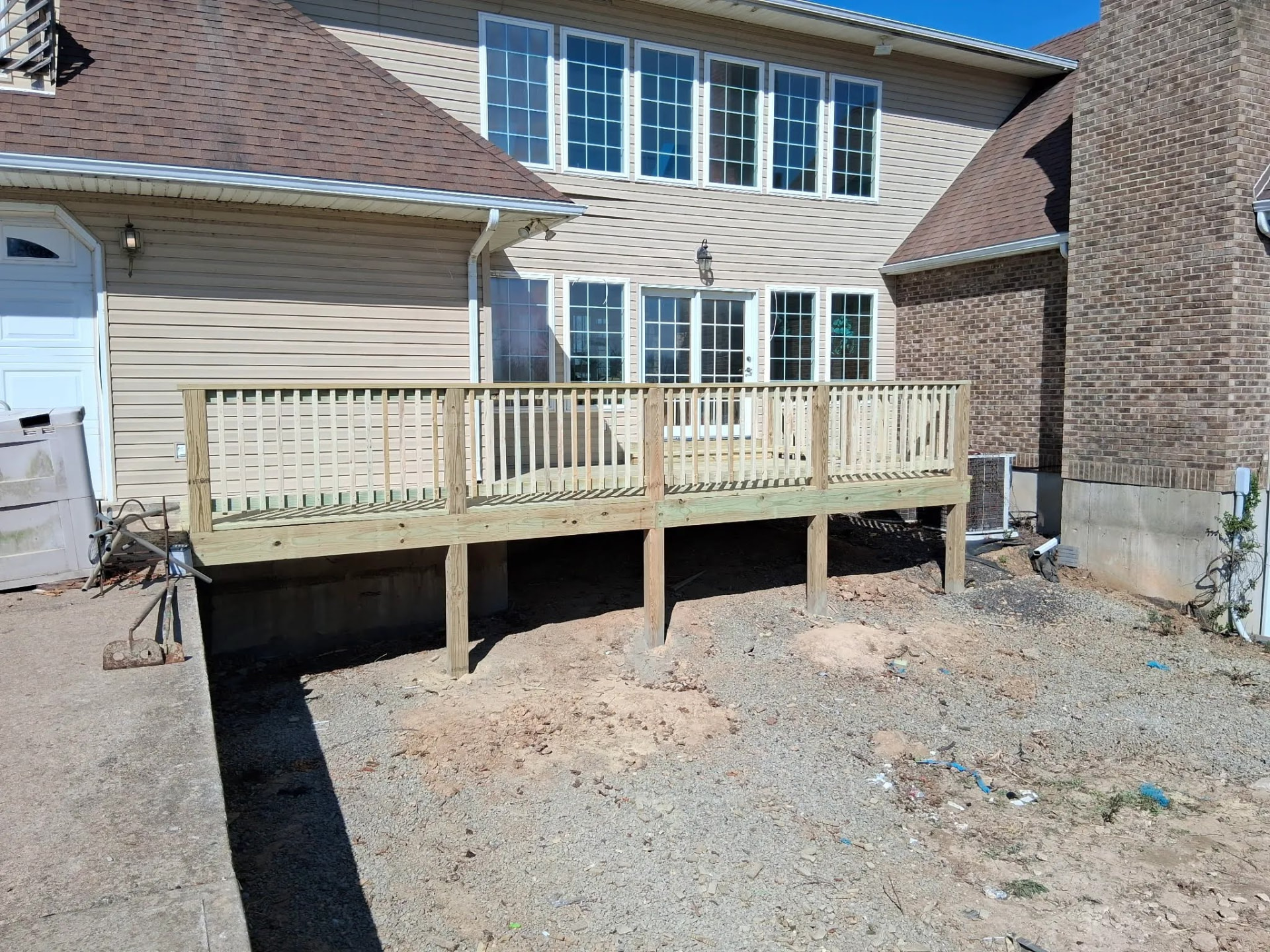 Newly built raised wooden deck with wood posts and balusters beside a home with tan siding and a brown shingle roof