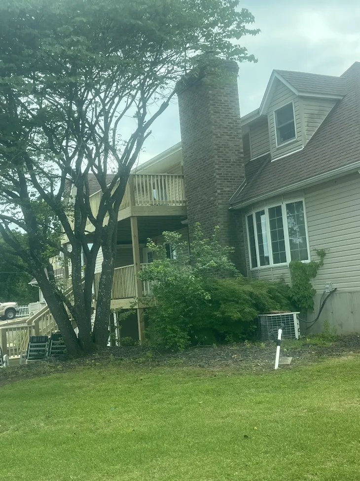 Multi-level wooden deck built off the side of a home with a brick chimney, mature trees, and a green lawn