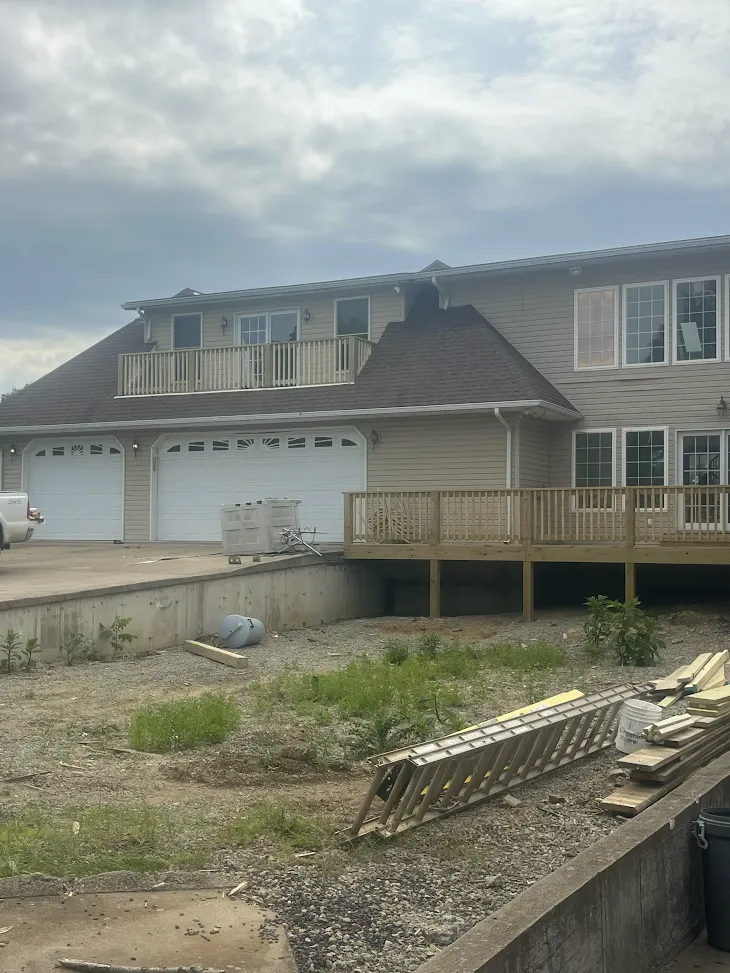 Home with a two-car garage, dormer balcony, and an elevated wooden deck during construction