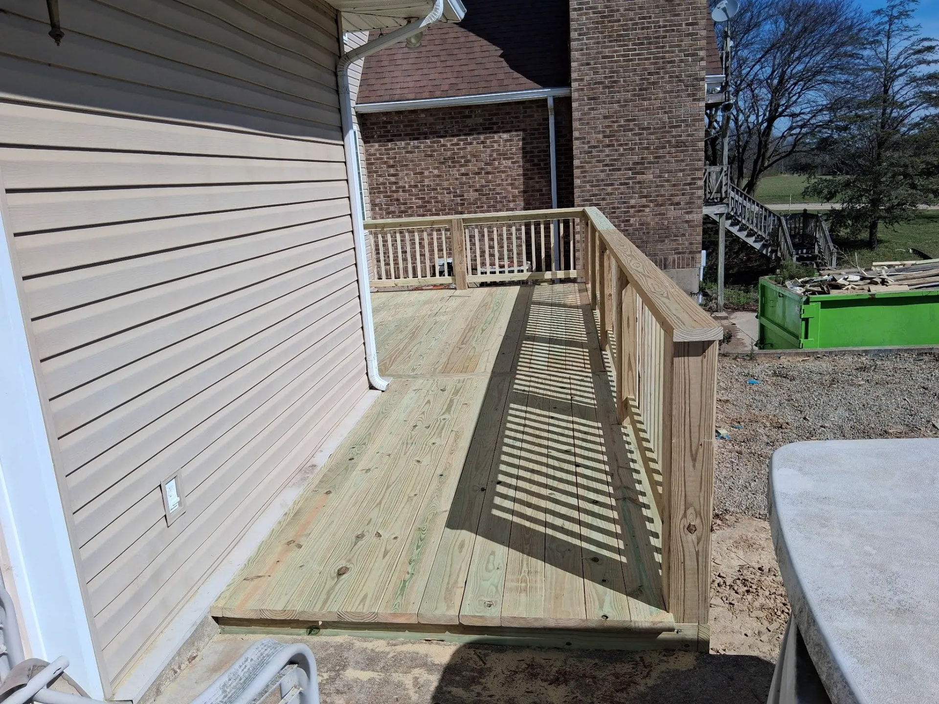 Walking surface of a newly built wooden deck with perimeter railing beside tan siding