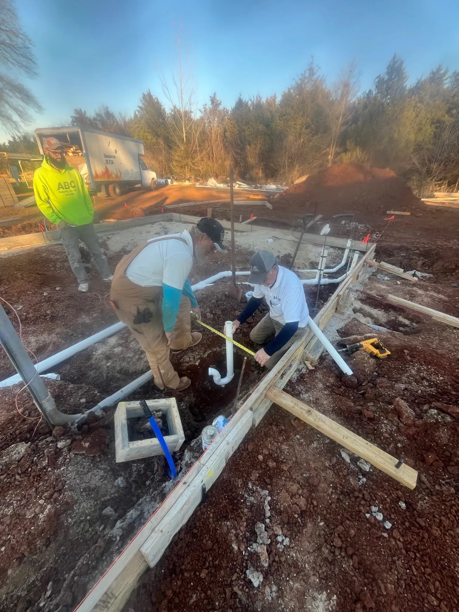 Workers measuring and setting plumbing pipes inside the slab forms