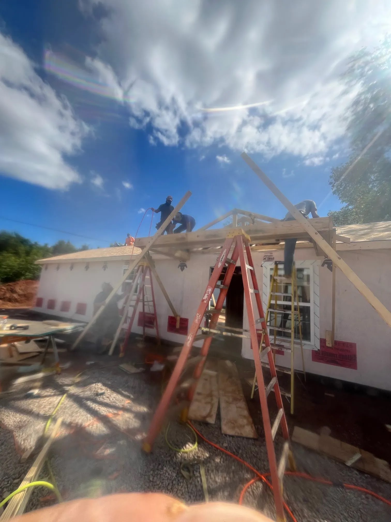 Crew on ladders framing a porch roof over a house with weather barrier