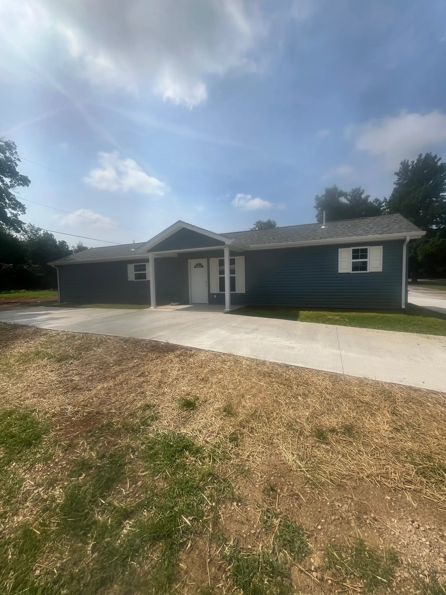 Completed blue ranch home with white trim, covered entry, and concrete driveway