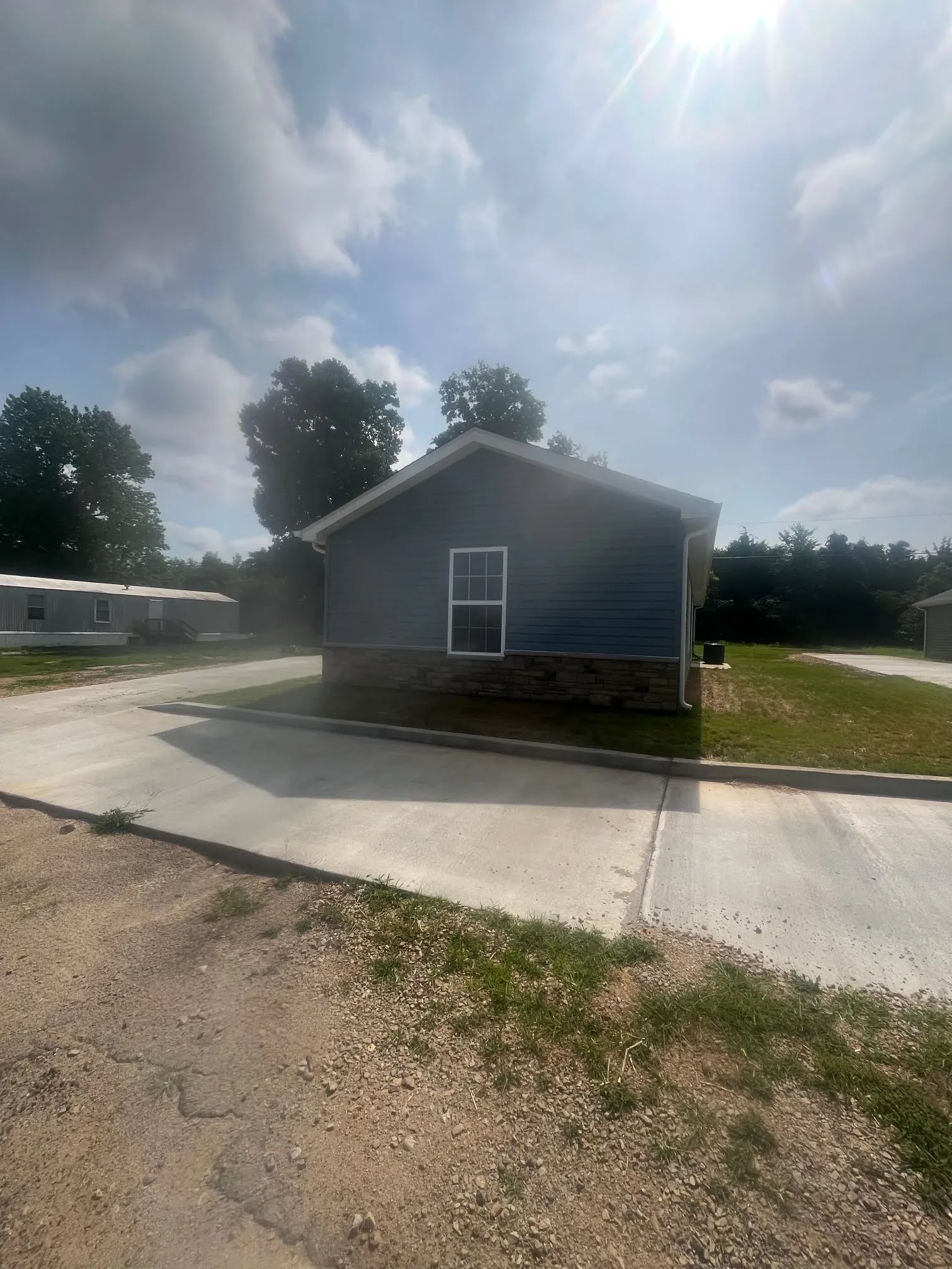 Side of a finished blue home with stone skirting, window, gutter, and driveway