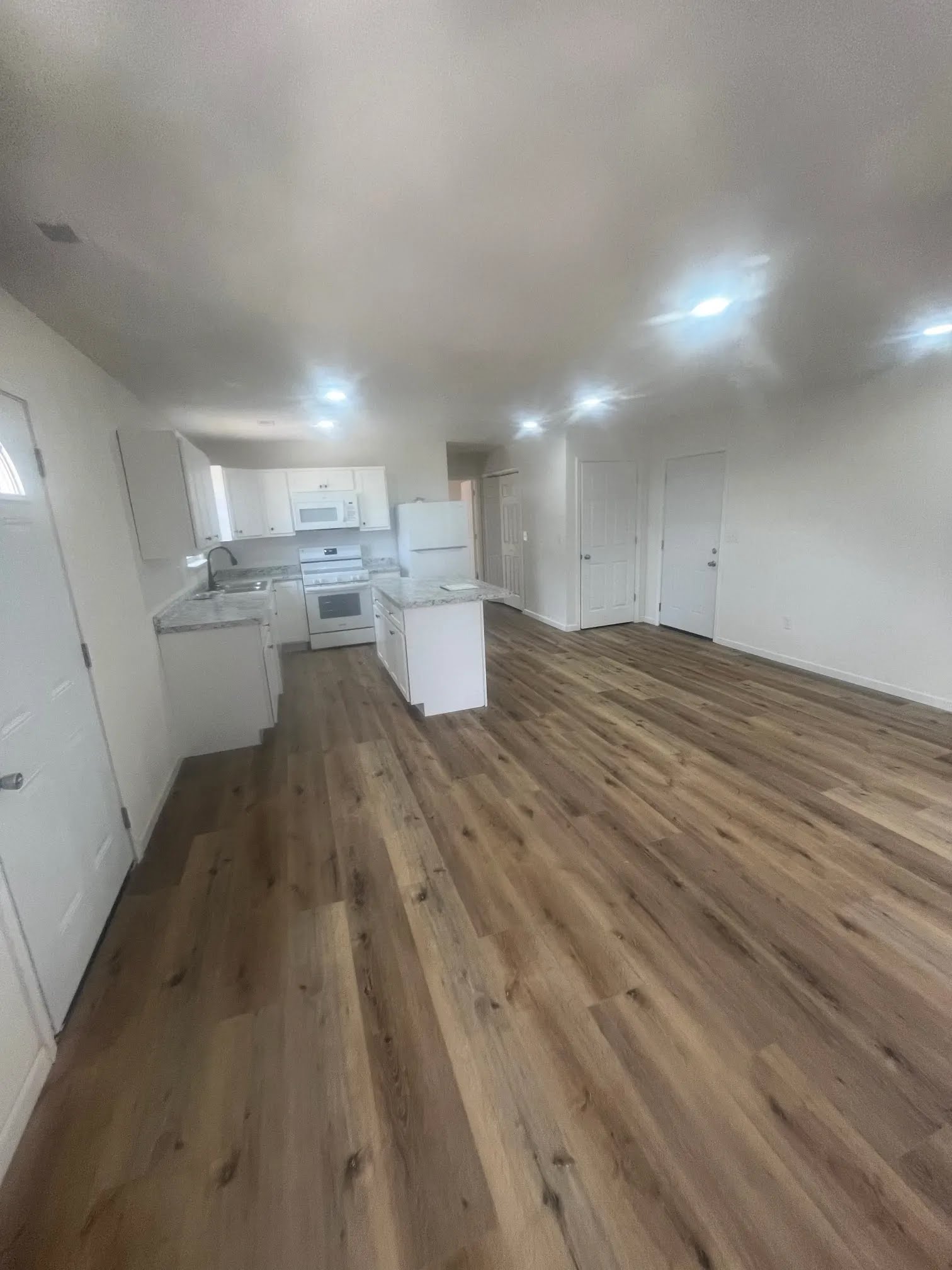 Open kitchen and living area with wood-look flooring, white cabinets, and island
