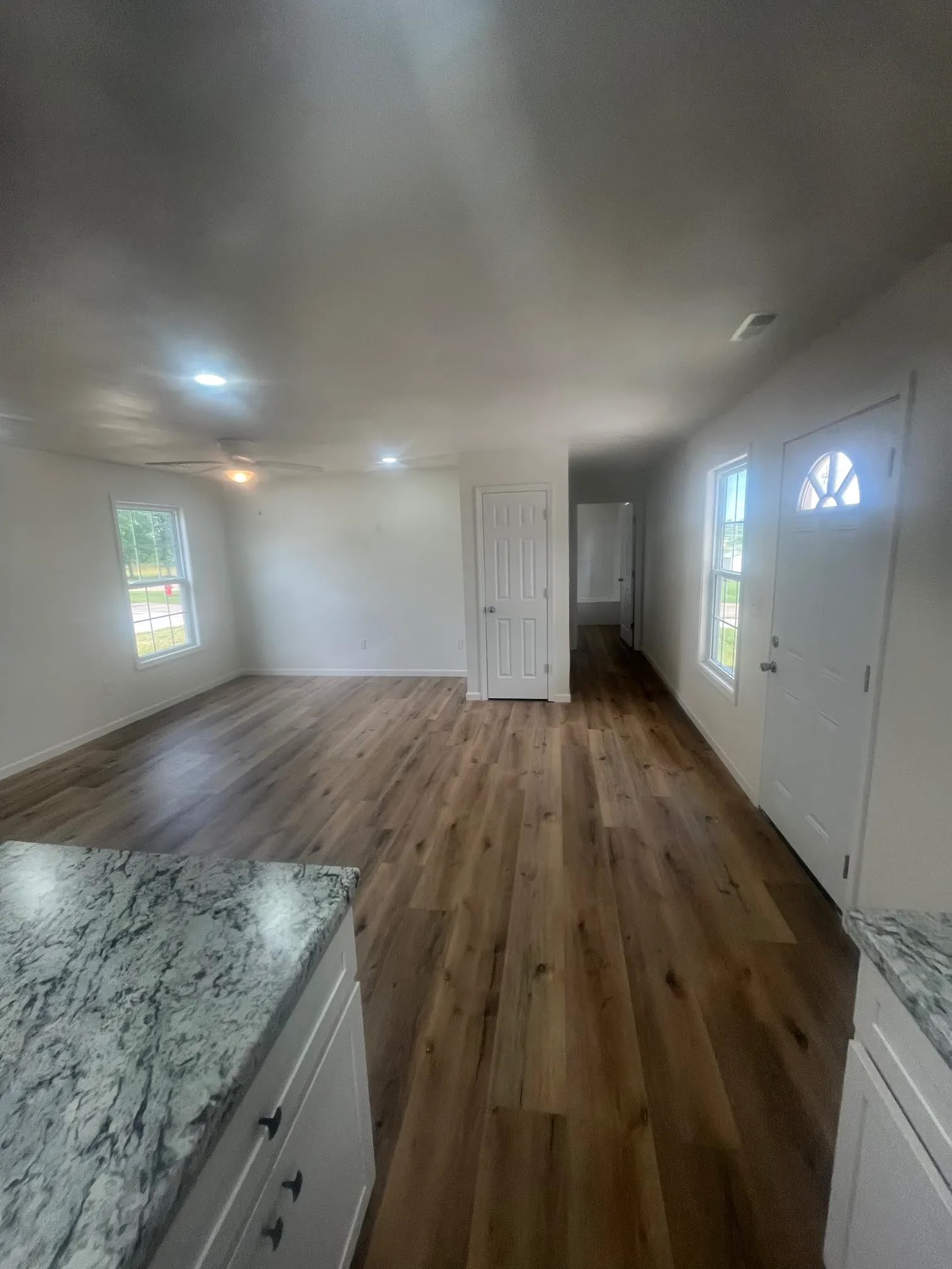Living room with wood flooring, white walls, windows, and front door