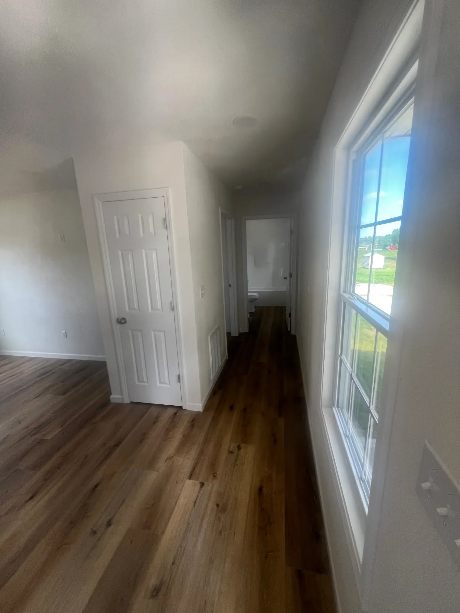 Hallway with wood flooring, windows, and interior doors leading to a bathroom
