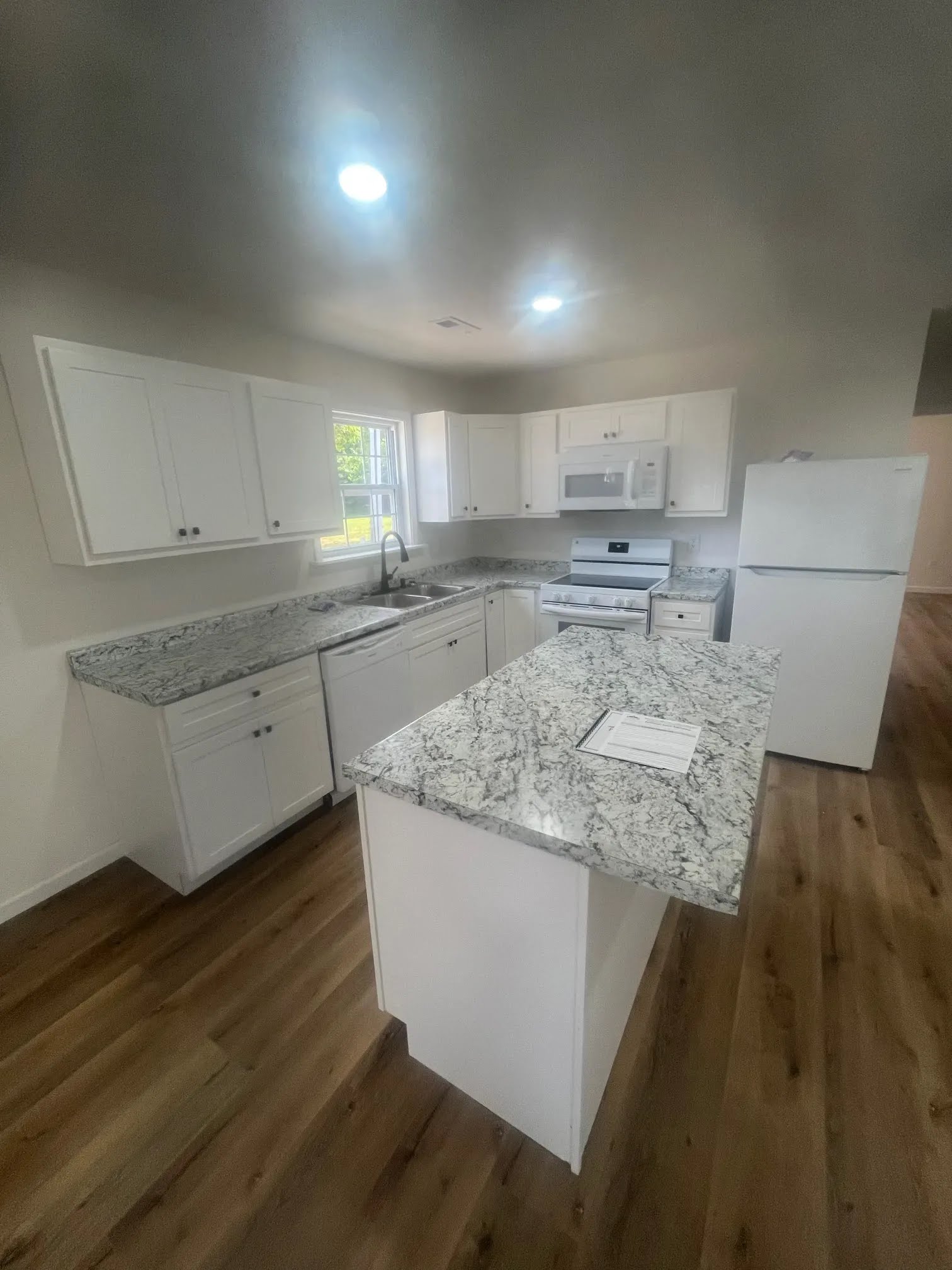 White kitchen with granite-look counters, island, appliances, and wood flooring