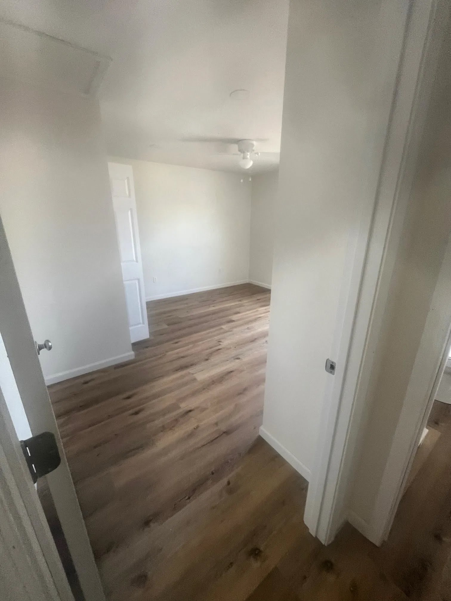 Bedroom with wood-look flooring, white walls, and a ceiling fan, seen from the doorway