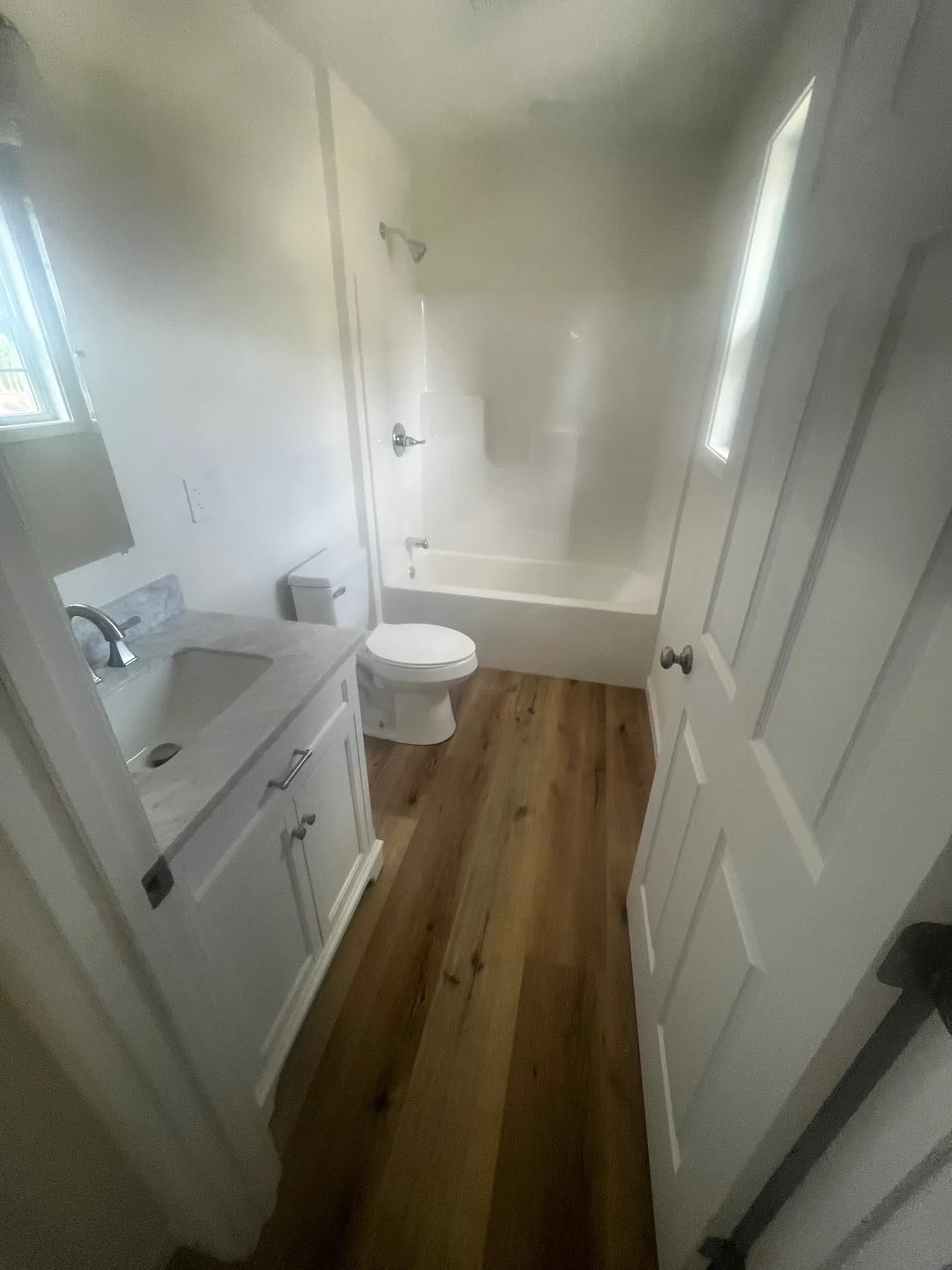 Bathroom with white vanity, tub and shower surround, toilet, and wood flooring