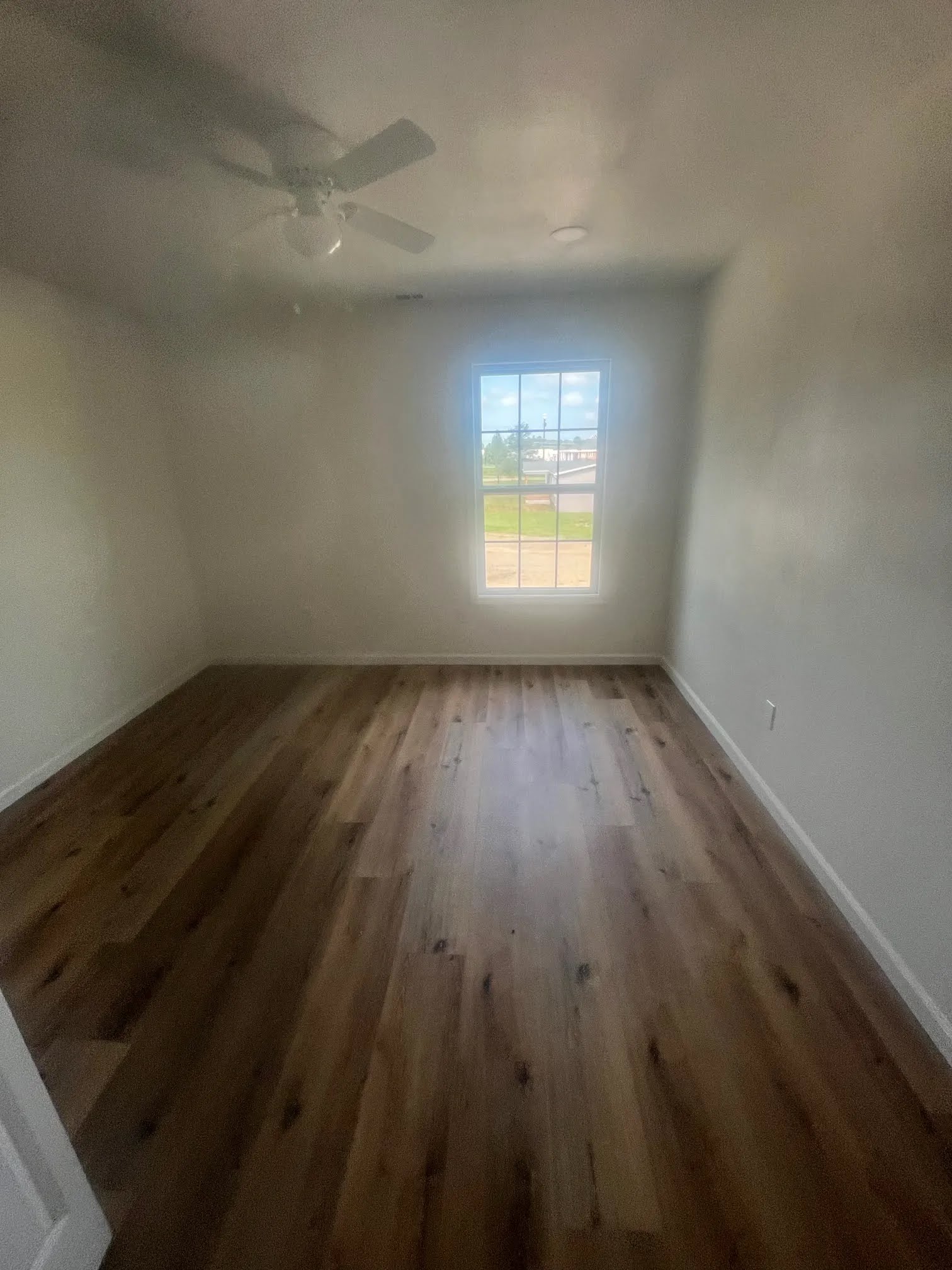 Empty bedroom with wood flooring, a ceiling fan, and a single window