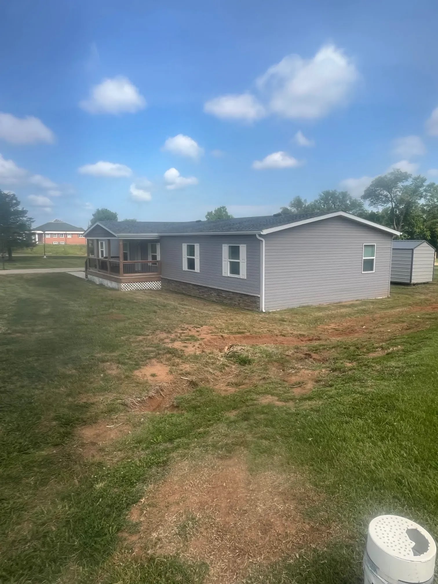 Gray home exterior with siding, gutters, stone skirting, and a front deck
