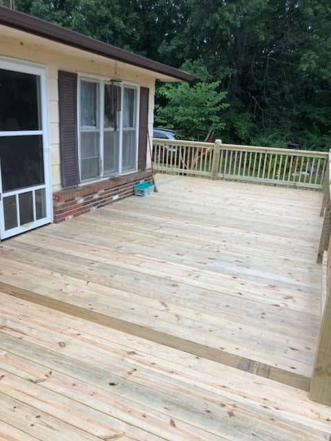 Multi-level wooden deck with railing beside cream siding and brick accents